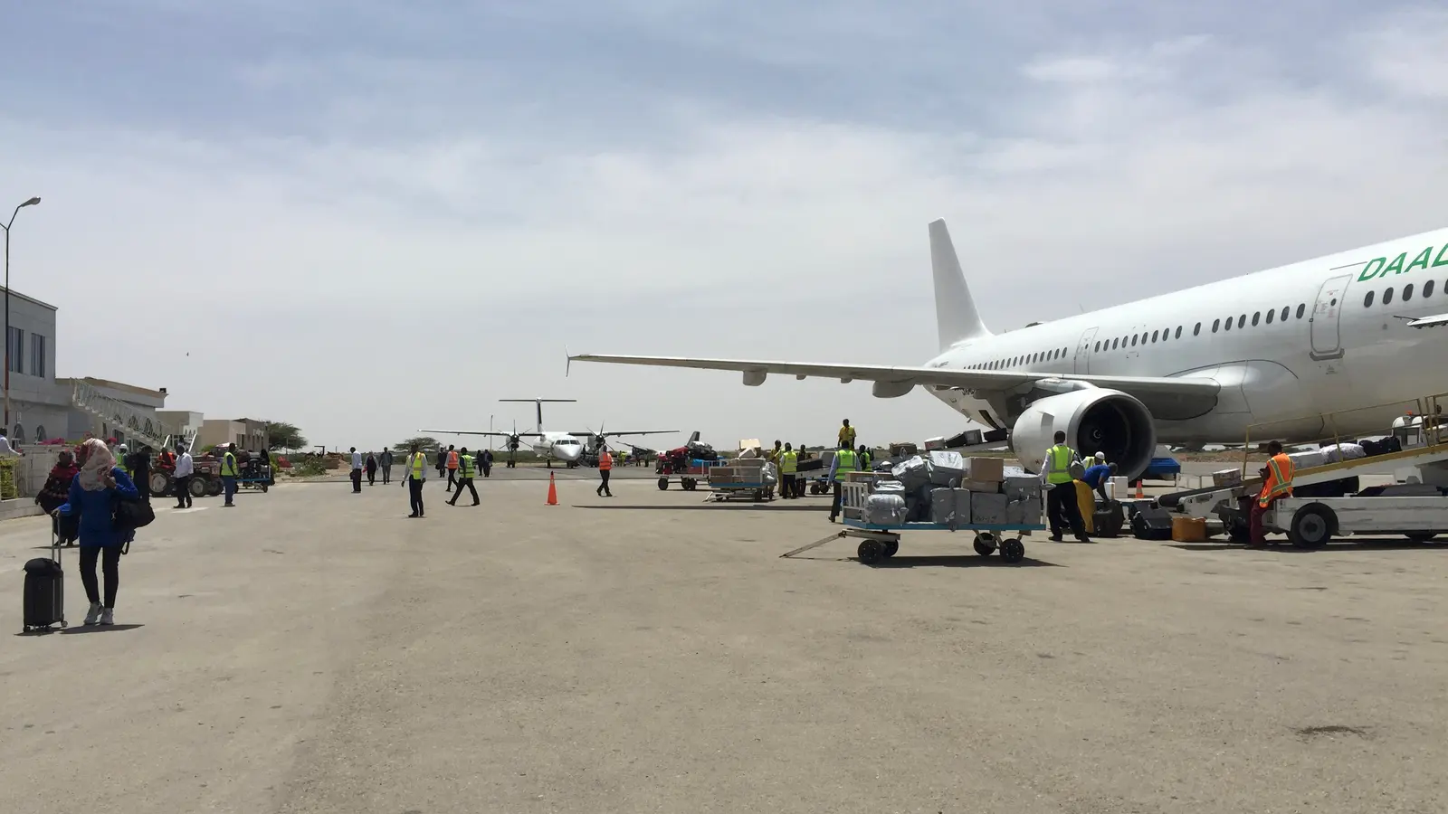 Passengers and baggage on the apron at Hargeisa airport beside a parked airliner