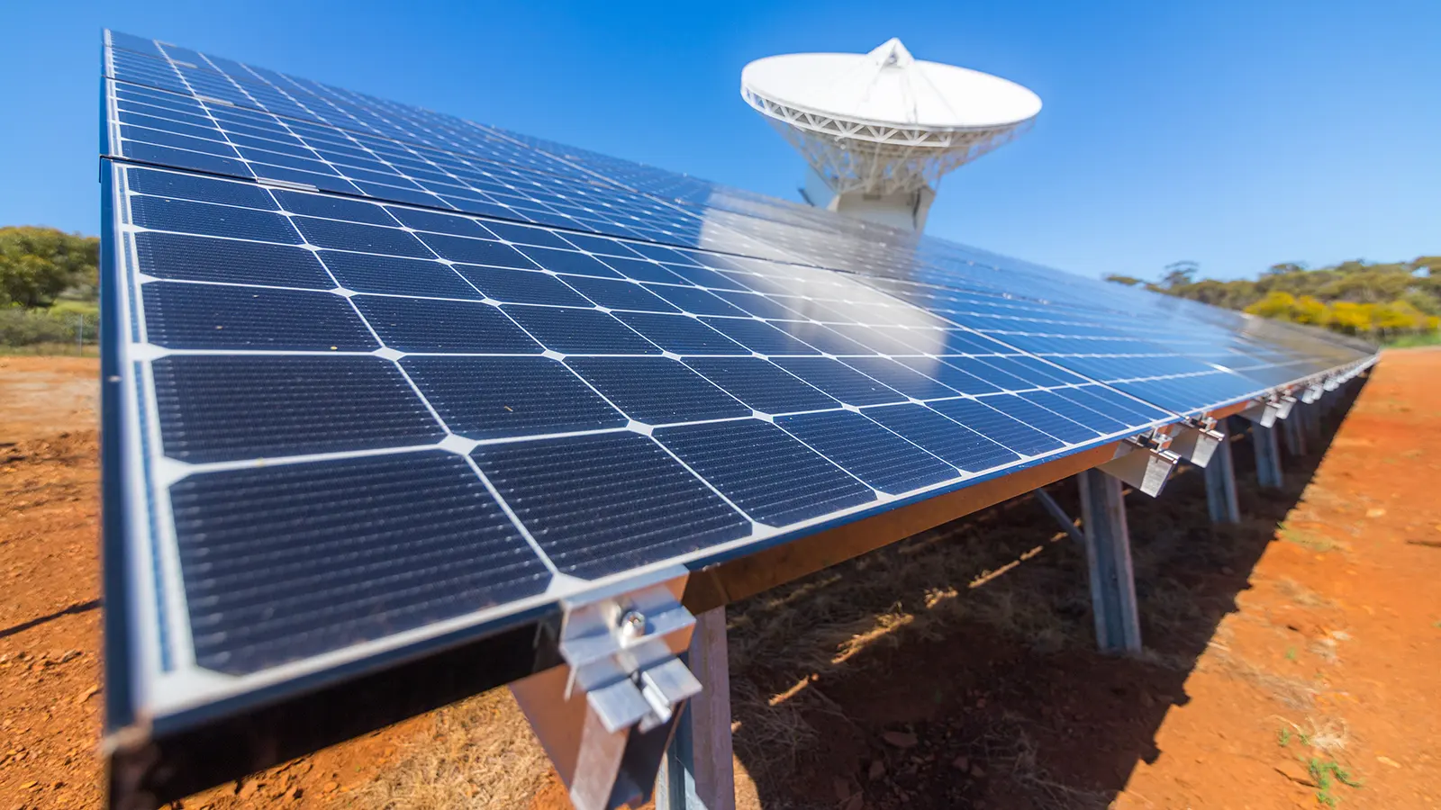 A ground-mounted solar panel array on red earth under a clear sky (New Norcia, Australia; illustrative)