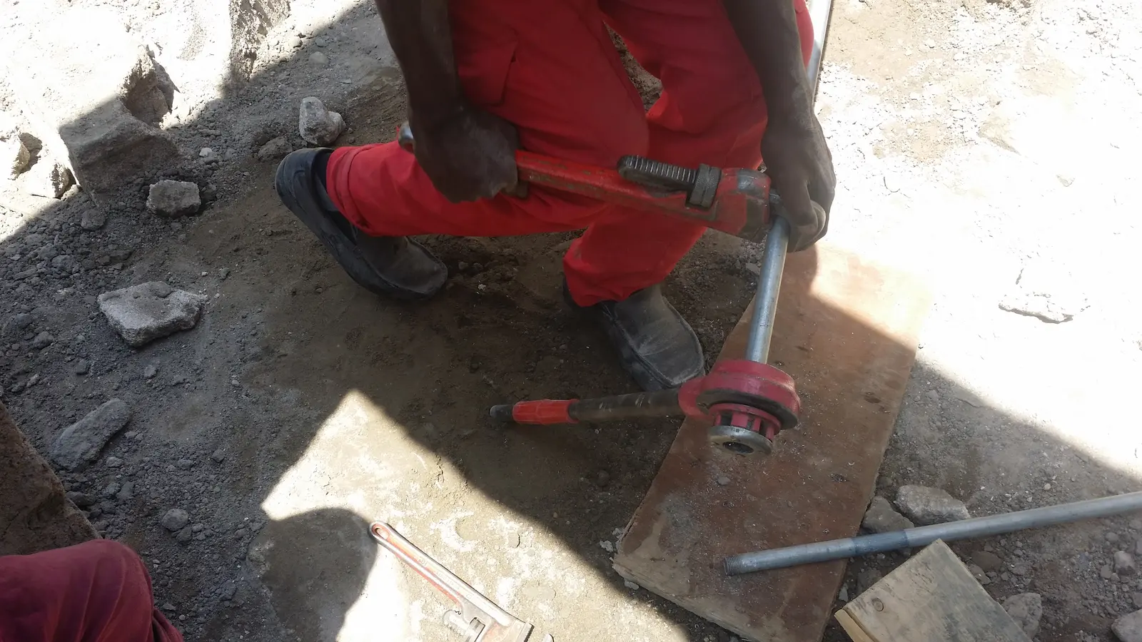 A plumber threading a steel pipe on a building site in Hargeisa