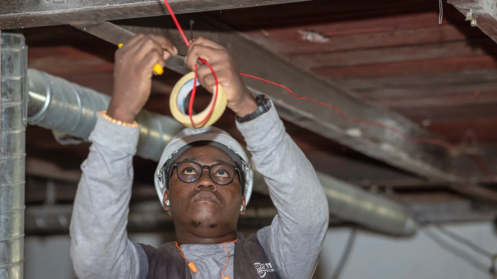 An electrician pulling cables through conduit under a ceiling