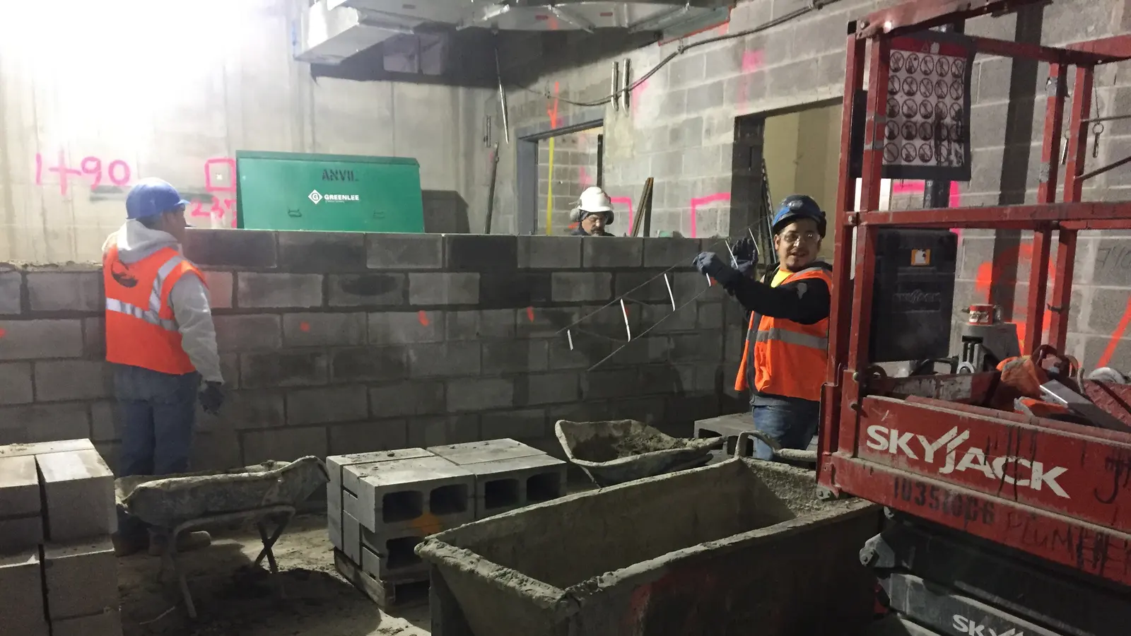 Masons laying a concrete block wall from a lift platform