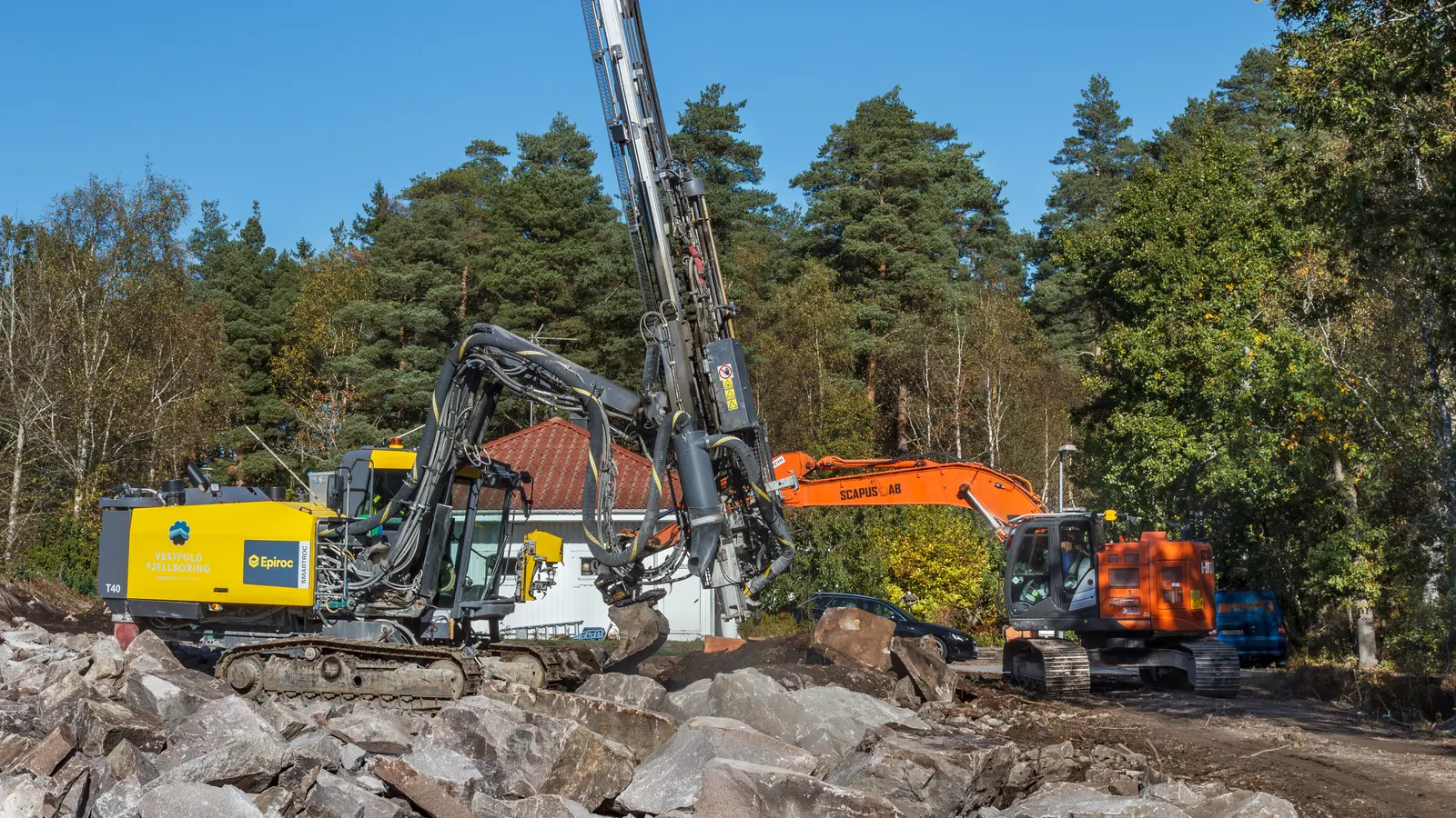 A surface drill rig and an excavator working on blasted rock